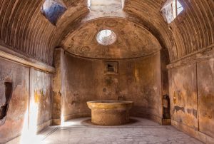 The interior of main public baths in ruins of Ancient Roman city Pompeii, Campania region, Italy. Sunny day. City destroyed by the eruption of Mount Vesuvius. Inside of Forum Baths. Big bowl for water