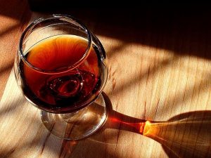 A glass of port wine sits in the sun and the glass reflects onto the table